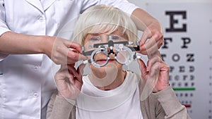 Optician holding phoropter, preparing for old woman vision examination, health