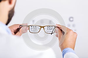 Optician holds glasses in front of eyesight test chart