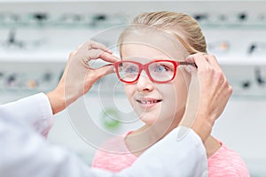 Optician putting glasses to girl at optics store