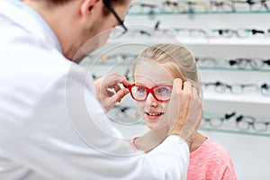 Optician putting glasses to girl at optics store