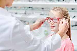 Optician putting glasses to girl at optics store