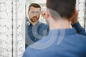 In Optics Shop. Portrait of male client holding and wearing different spectacles, choosing and trying on new glasses at