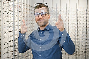 In Optics Shop. Portrait of male client holding and wearing different spectacles, choosing and trying on new glasses at