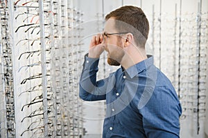 In Optics Shop. Portrait of male client holding and wearing different spectacles, choosing and trying on new glasses at