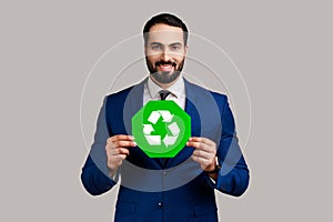 Optimistic bearded businessman holding green recycling sign, saving environment.