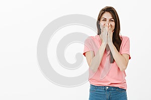 Optimistic carefree attractive woman with long brown hair, chuckling and covering mouth with palms, trying not to laugh
