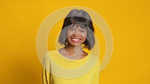 Optimistic dark skinned young woman laughs out loudly on yellow background