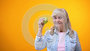 Optimistic elderly lady biting fresh green apple, healthy teeth, stomatology