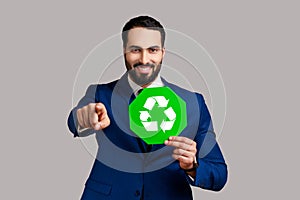 Optimistic man holding green recycling sign, saving environment, ecology concept, pointing to camera
