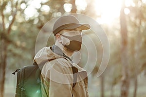 Optimistic man in medical mask walks through park with backpack