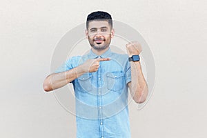 Optimistic man pointing at his smart watch, looking at camera, warning about deadline.