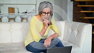 Optimistic mature middle-aged woman spends leisure time at home using laptop