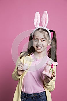 Optimistic small kid posing with painted eggs and a pink rabbit toy