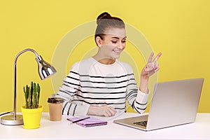 Optimistic woman office manager showing victory gesture and smiling looking into laptop screen.