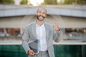 Optimistic young businessman giving thumb up while posing outdoors