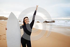 Optimistic young woman posing with surfboard, ready for going to catch a wave, having fun on the beach, free space