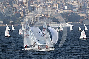 Optimists and two lazers are racing in ÃÂ°zmir Gulf and ÃÂ°zmir city view is behind.