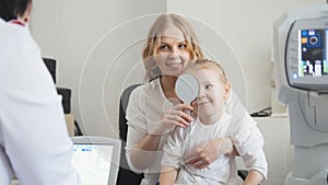 Optometrist checks child`s eyesight - mother and child in ophthalmologist room