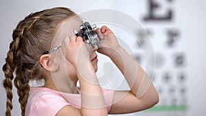 Optometrist putting phoropter on little girl, child complaining to see nothing