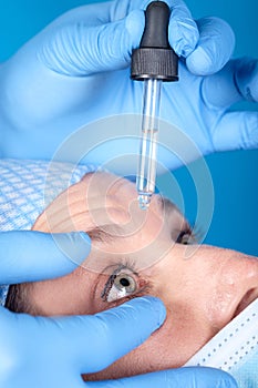 Optometrist throwing in liquid medication into  a females blue eyes