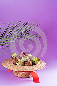 Opuntia fruit in a straw hat with a palm leaf on a trendy purple background. Prickly pear or Fichi Dindia Salento, Puglia. photo