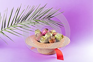 Opuntia fruit in a straw hat with a palm leaf on a trendy purple background. Prickly pear or Fichi Dindia Salento, Puglia. photo