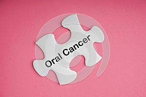ORAL CANCER text with white jigsaw puzzle on pink background
