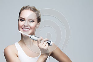 Oralcare and Dentistry Concepts. Caucasian Blond Woman Cleaning Teeth with Electric  Toothbrush Posing Against Over Gray