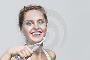 Oralcare and Dentistry Concepts. Caucasian Blond Woman Cleaning Teeth with Electric  Toothbrush Posing Against Over White