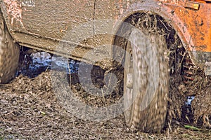 Orange 4x4 off-road car ride through mud, wheels slip and dirt flies