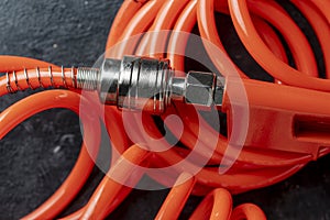 An orange air hose with an hose coupling on a black background, closeup. Detail of air compressor hose and pistol