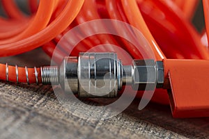 An orange air hose with an hose coupling on a wooden background, closeup. Detail of air compressor hose and pistol