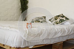 Orange alarm clock placed on white bed in bright bedroom