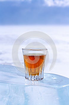 An orange alcoholic drink in a glass stands on an ice piece.