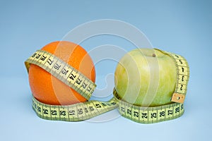 Orange and apple with measuring tape wrapped around them on the blue