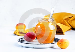 Orange Apricot jam or confiture in glass jar with spoon and fresh fruits on gray table background