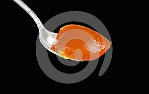 Orange or apricot jam in orange color on metal spoon isolated on black background closeup
