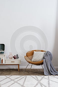 Orange armchair with plaid near sideboard against wall