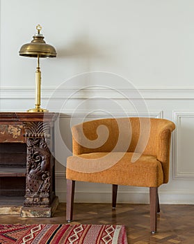 Orange armchair and wooden vintage ornate sideboard and lamp