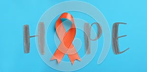 Orange awareness ribbon and word HOPE on light blue background, top view. Banner design
