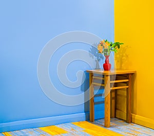 Orange azalea rhododendron flower in a tiny vase on a stool in a corner in super bright and contrast room with yellow blue painted