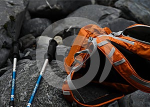 Orange backpack and blue walking sticks on rocks