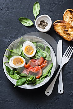 Delicious brunch - spinach, smoked salmon, soft boiled egg on a dark background, top view. Healthy eating diet