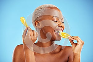 Orange, beauty and nutrition with a model black woman in studio on a blue background biting fruit. Food, skincare and