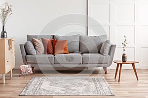 Orange and beige pillows on grey comfortable couch in chic living room interior