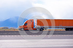 Orange big rig semi truck with long semi trailer running on the