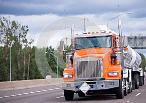 Orange big rig semi truck tractor with two tank trailers transporting fuel on the highway road