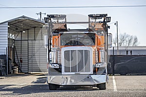 Orange and black car hauler big rig semi truck with empty semi trailer standing on the warehouse parking lot