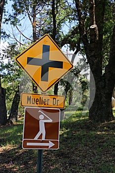 Orange and black road crossing sign with a brown and white sign with a man swinging a golf club.