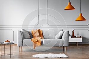 Orange blanket on grey scandinavian sofa, copy space on grey living room wall